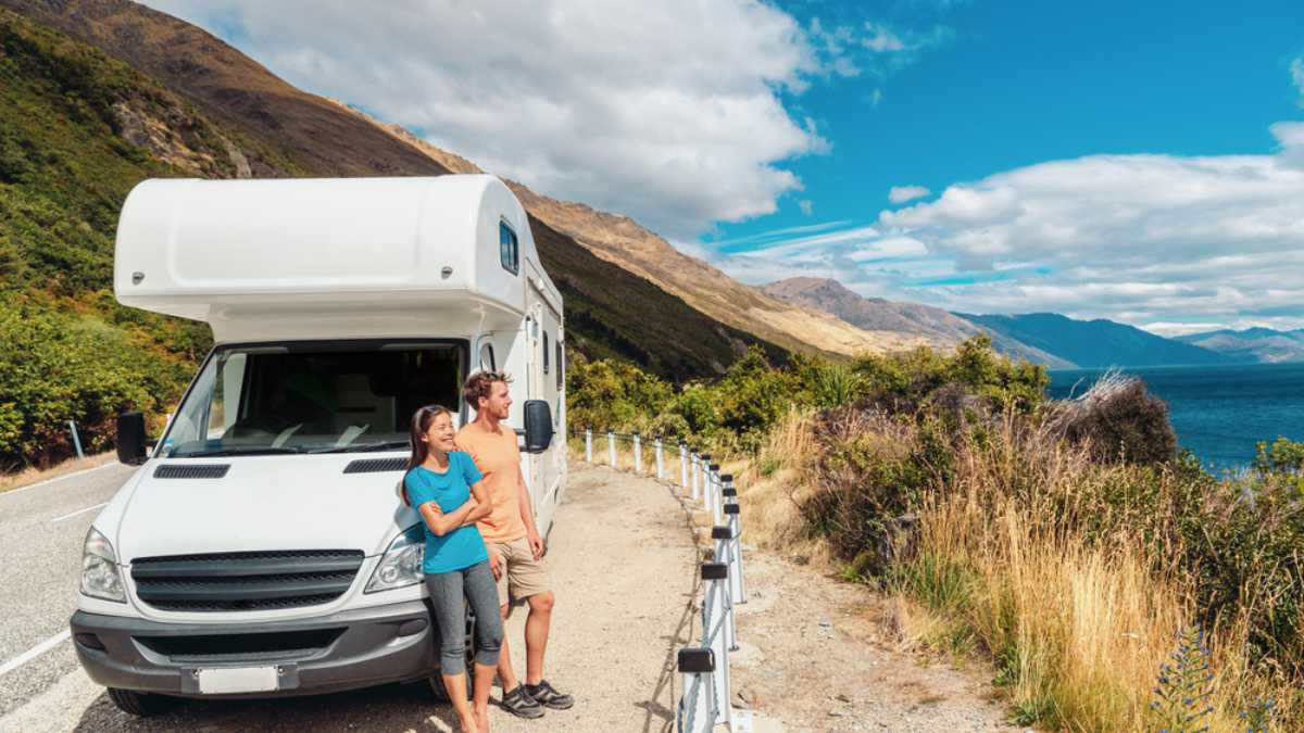 Motorhome RV camper van road trip on New Zealand. Young couple on travel vacation adventure. Two tourists looking at Lake Pukaki and mountains on enjoying view and break next to rental car