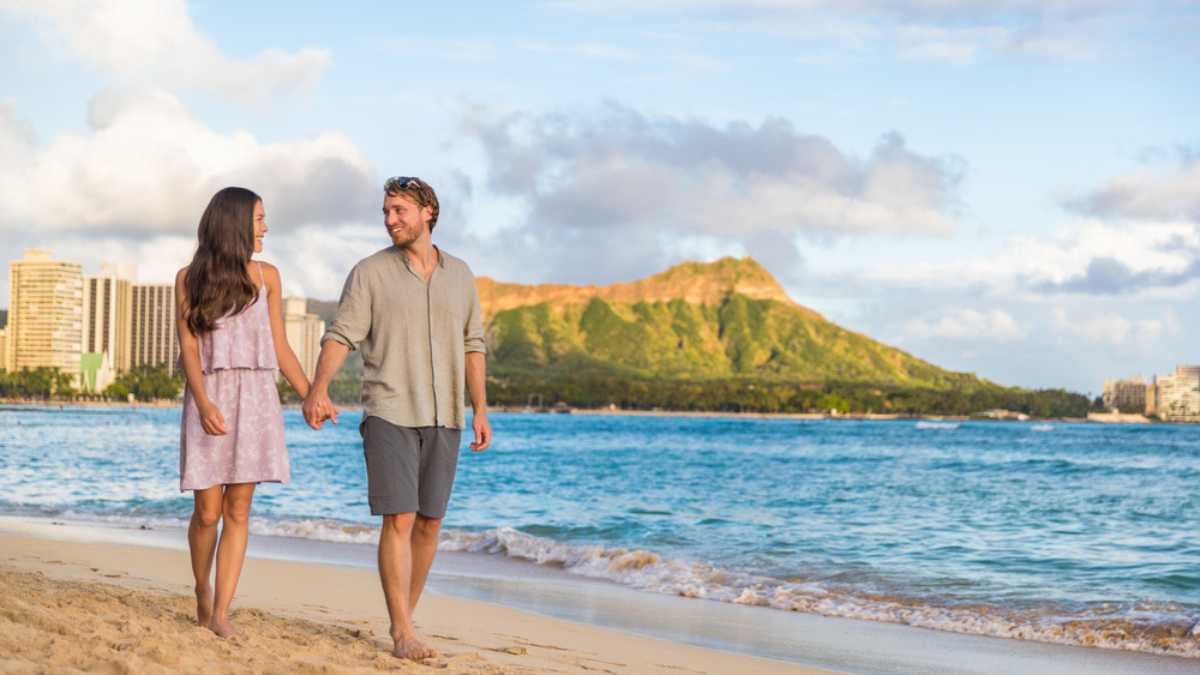 Couple walking on Waikiki beach Hawaii vacation. Happy couple in love relaxing at sunset on tourist famous travel destination in Honolulu, Oahu, Hawaii.