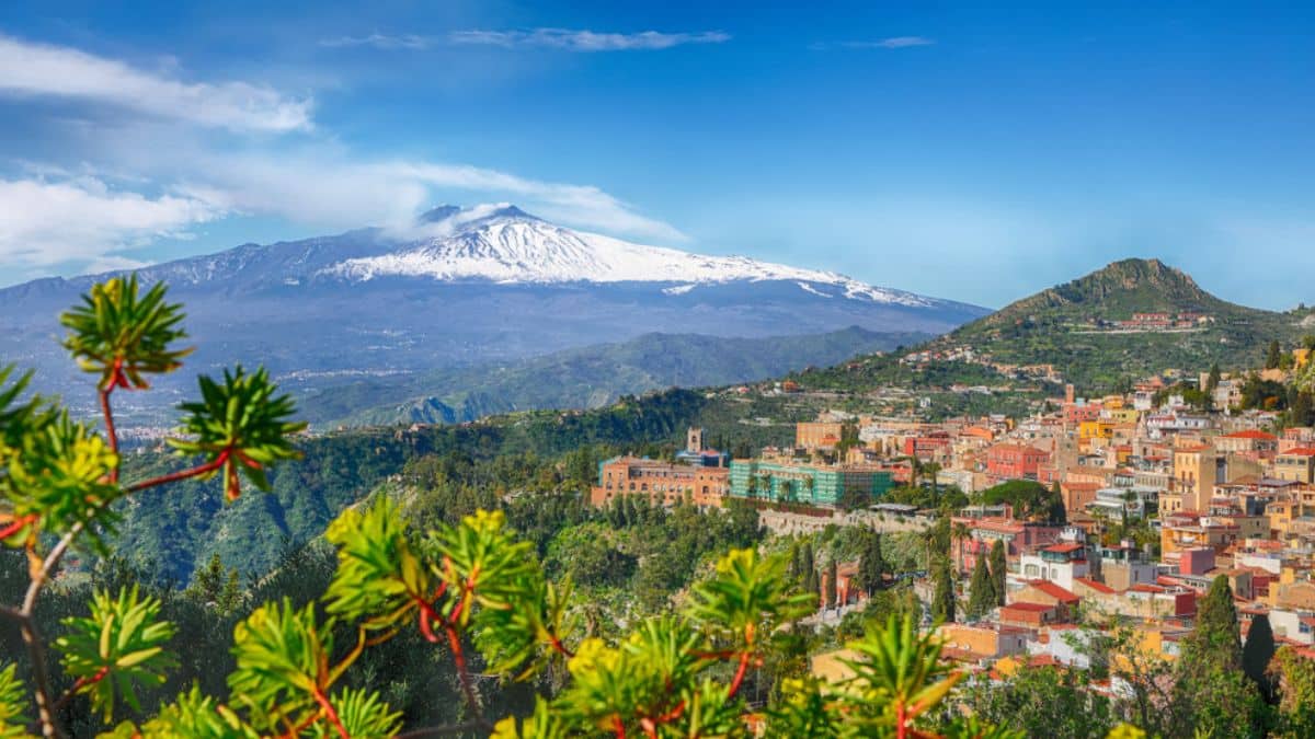 Etna volcano and Taormina town aerial panoramic view. Roofs of a lot of buldings. Smoking snow-capped Mount Etna volcano. Taormina, Sicily, Italy.