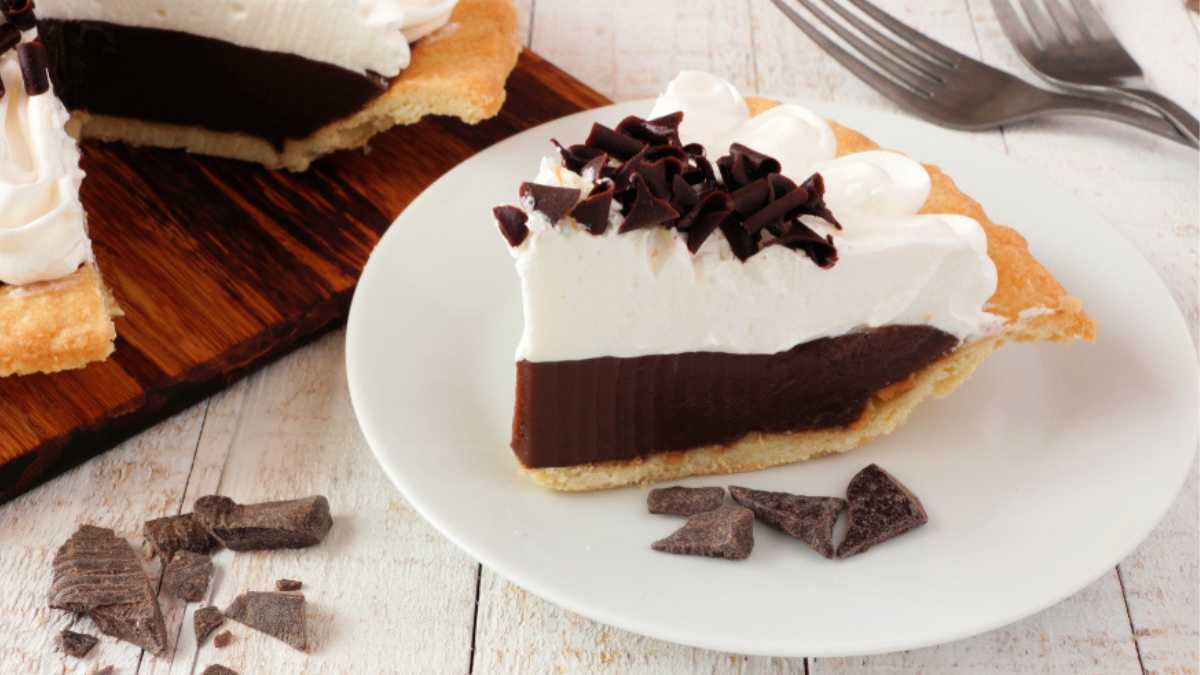 Slice of sweet chocolate cream pie. Close up table scene with a white wood background.