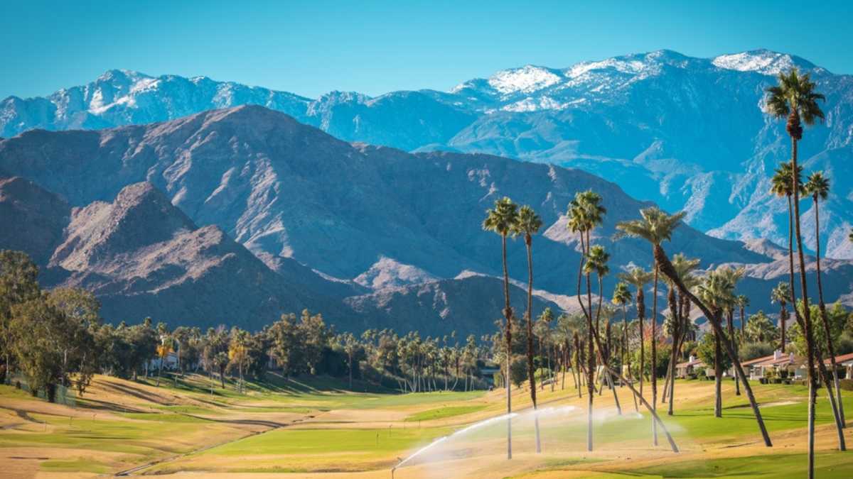 Sunny Warm Winter Time in the Palm Desert Coachella Valley. Golf Courses, Palms and Mountains Covered by Fresh Snow. Recreation in Southern California State, United States of America.