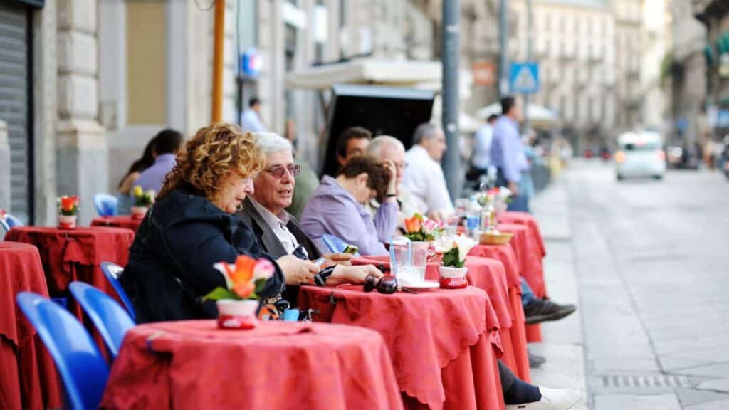 Tourists and locals sitting in outdoor cafe on busy street in the center of Milan, a metropolis in Italy's northern Lombardy region. Milan, Lombardy, Italy.