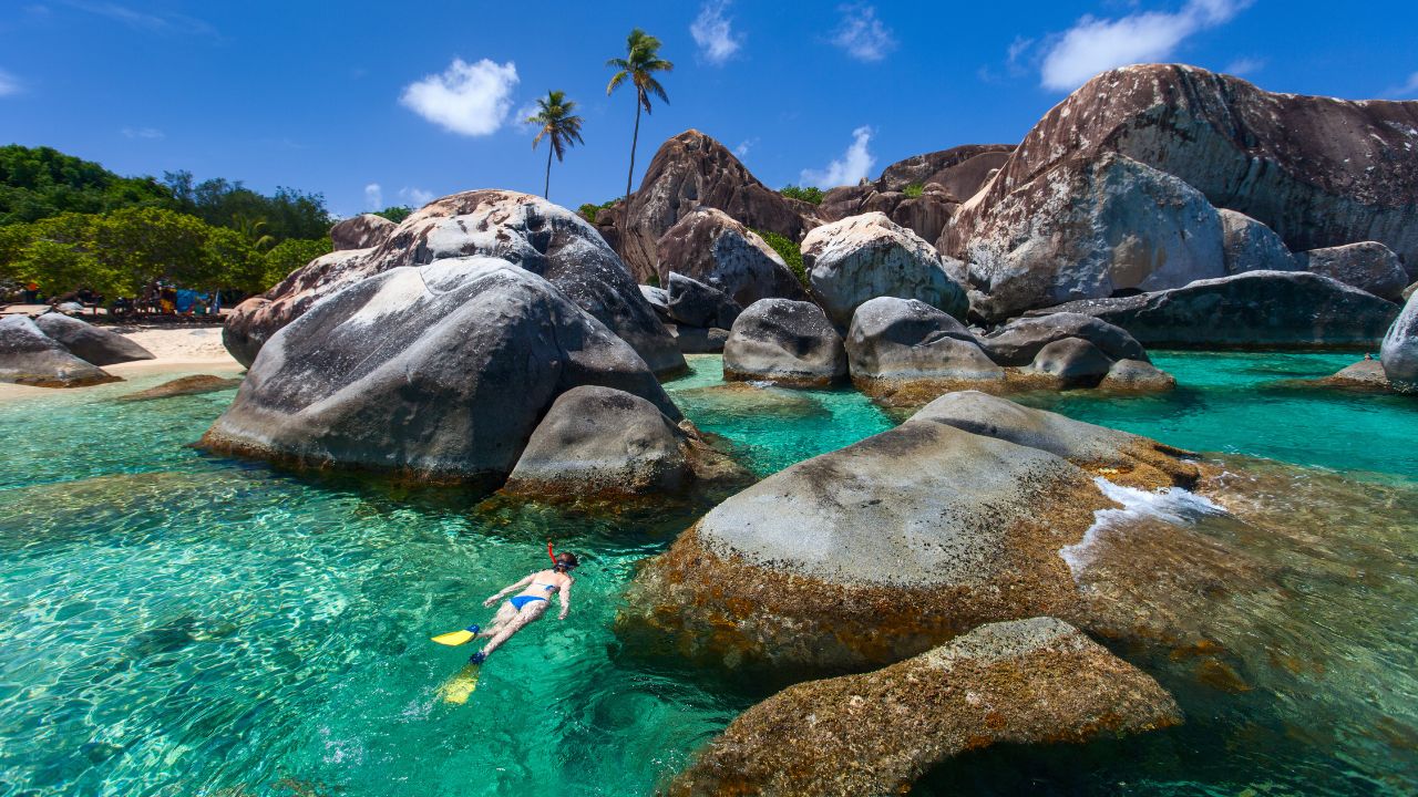 Young woman snorkeling in turquoise tropical water among huge granite boulders at The Baths beach area major tourist attraction on Virgin Gorda, British Virgin Islands, Caribbean