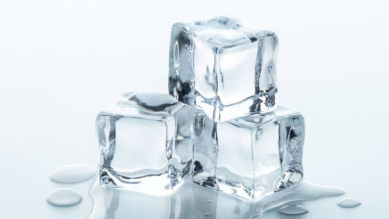 Melting Ice cubes with water drops on a table. Clear ice in cube shape. Frozen water. Ice maker. Fake or Artificial acrylic or plastic ice cubes. White light blue background.