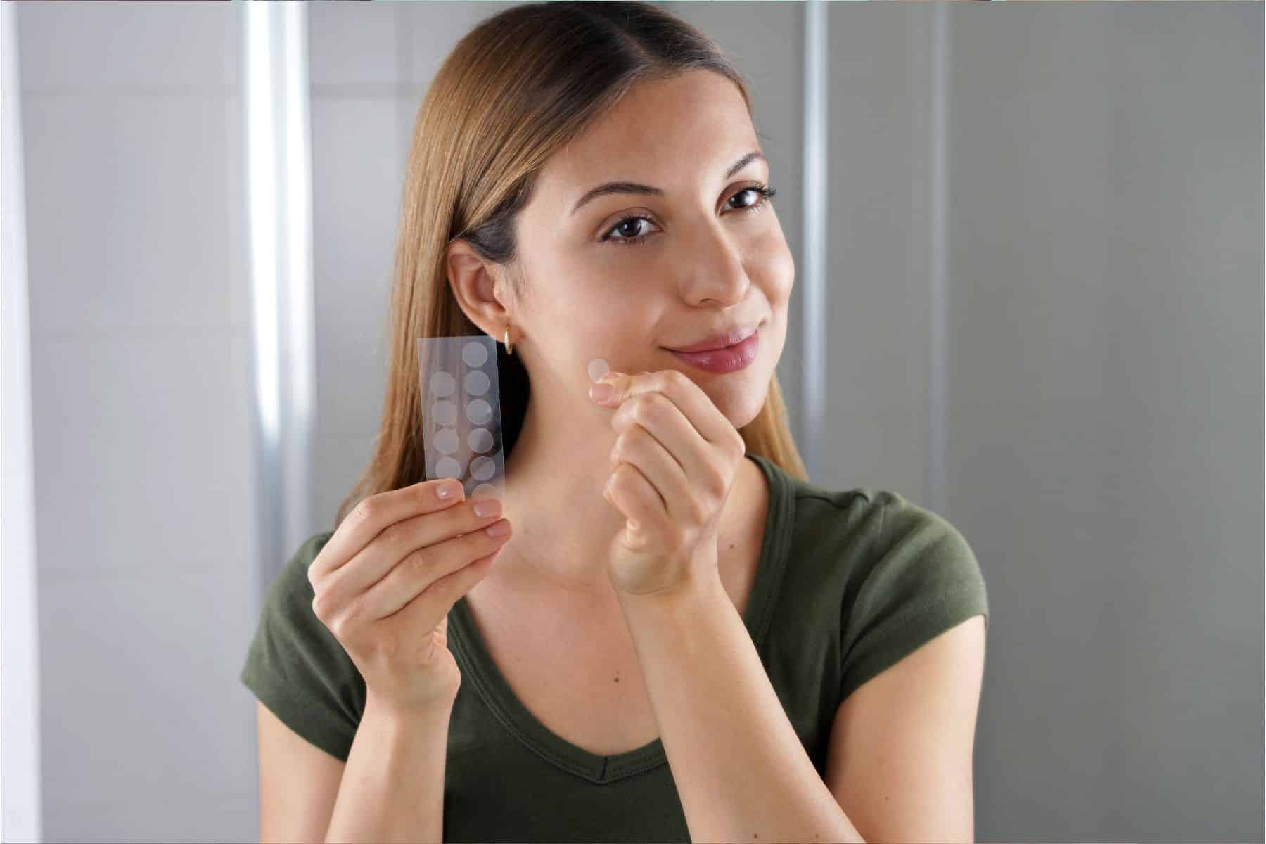 Beauty girl applying acne treatment anti-pickel patch on a pimple in bathroom at home