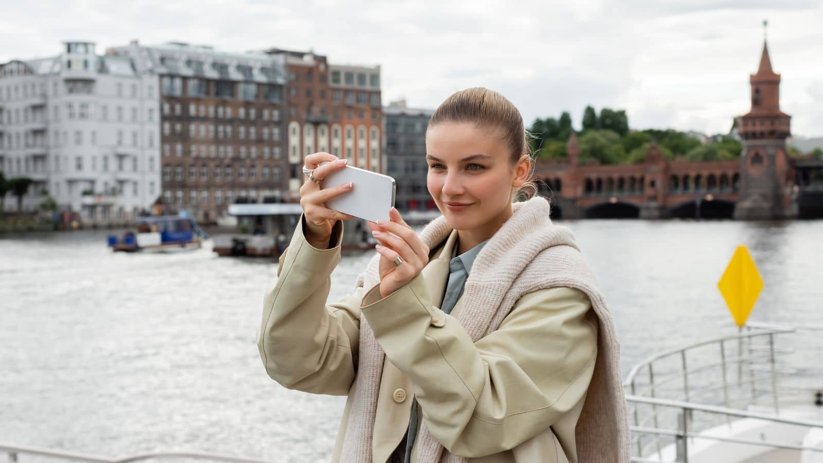 Smiling woman in trench coat taking selfie in Berlin city